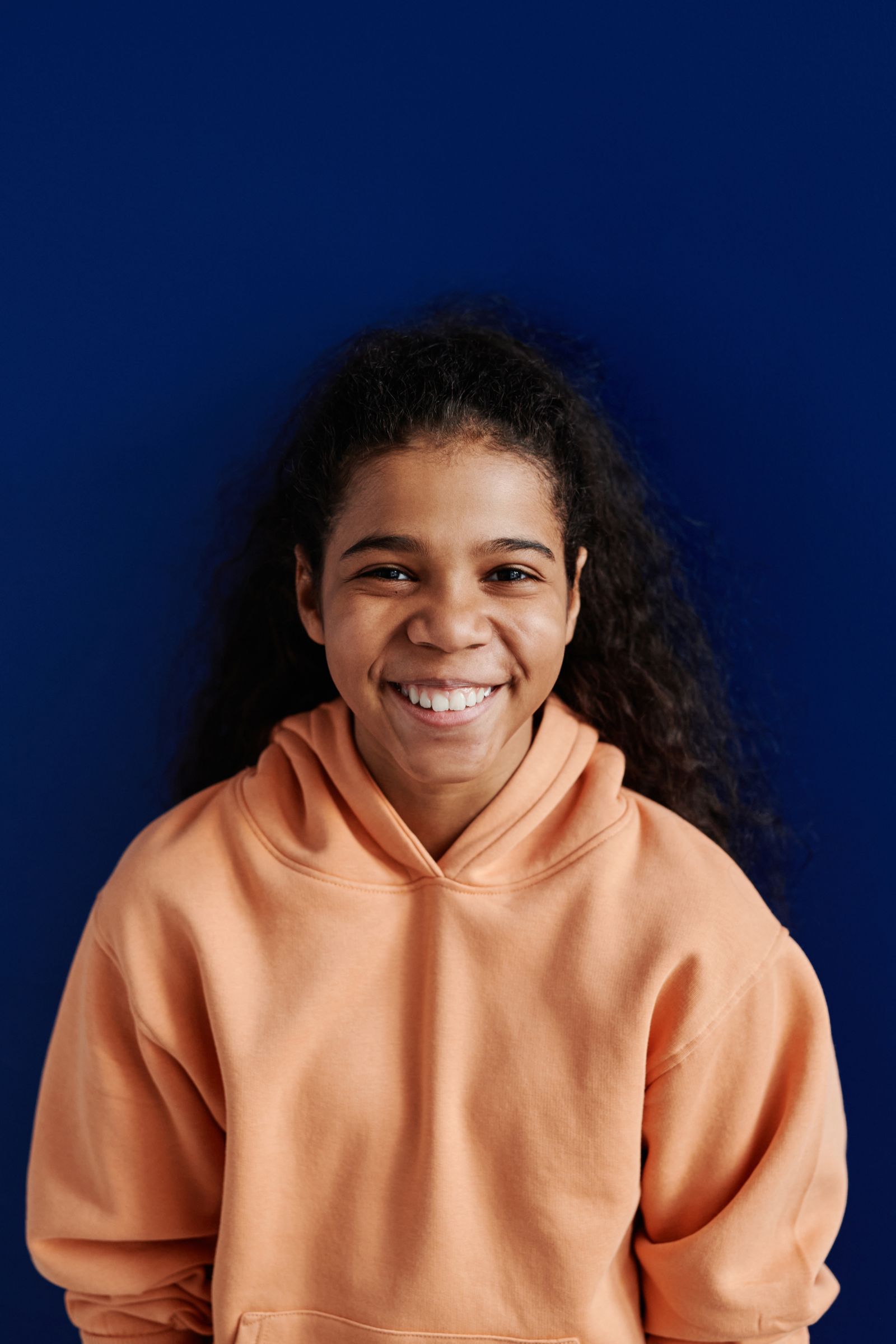 Teen in an orange hoodie with a bright, confident smile